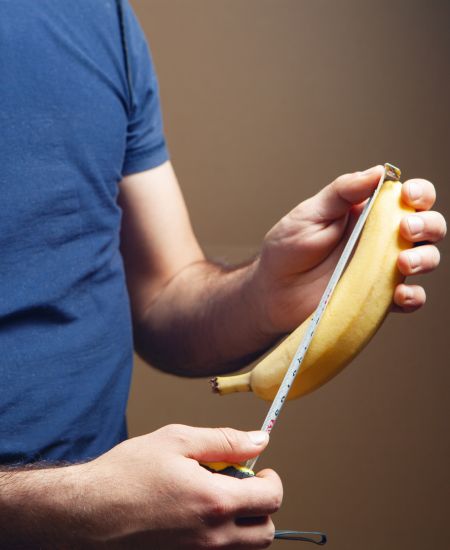 A man in a blue shirt holds a measuring tape next to a banana.