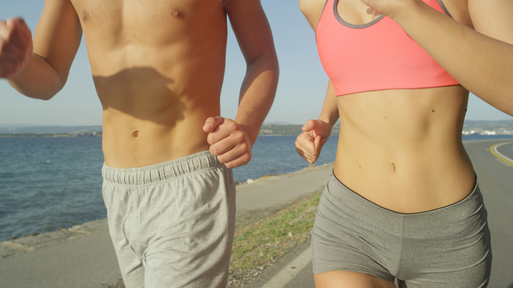 Man and woman running on a beach with only their midsections in view